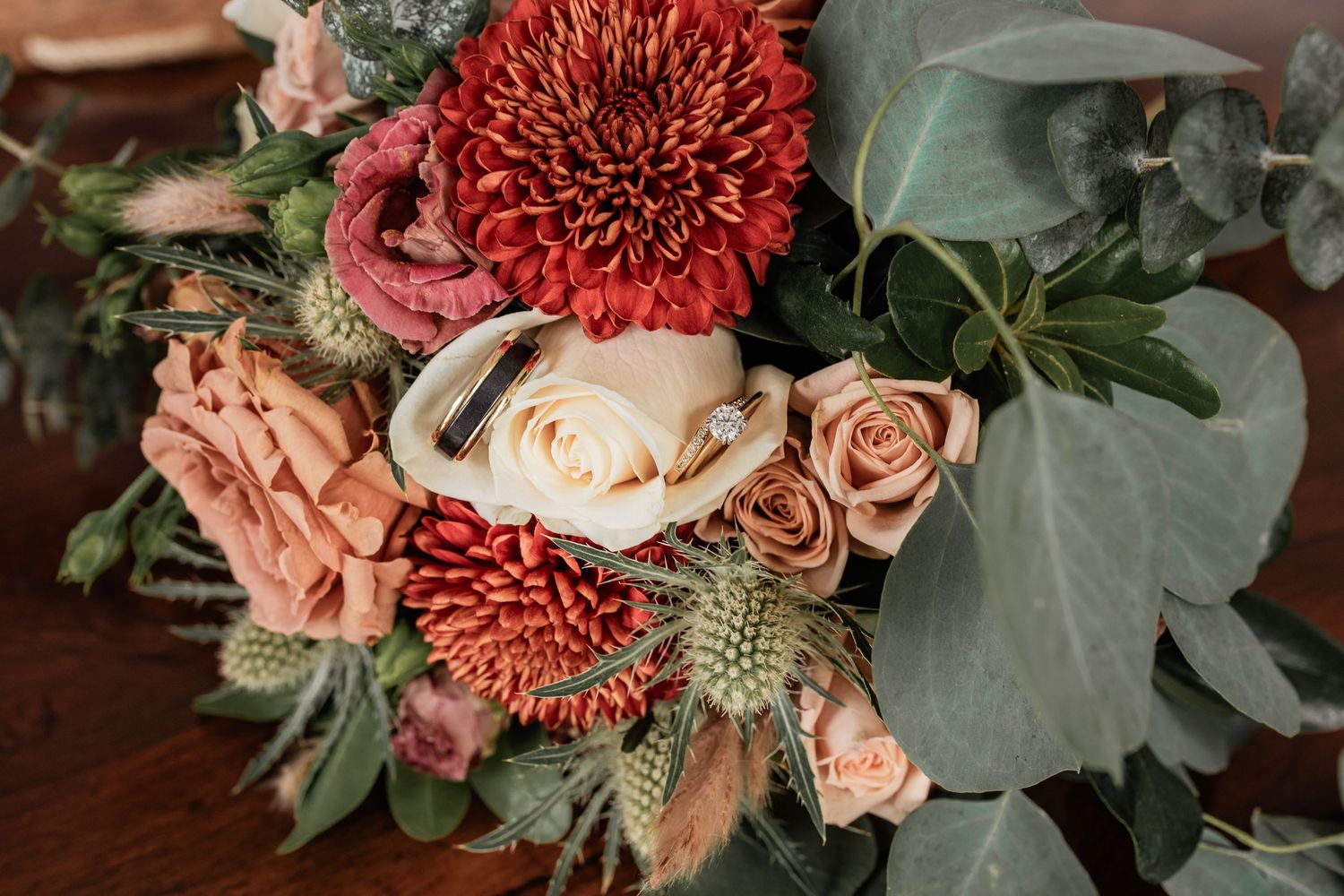 Wedding bouquet with coral dahlias, roses, and eucalyptus leaves on wooden surface.