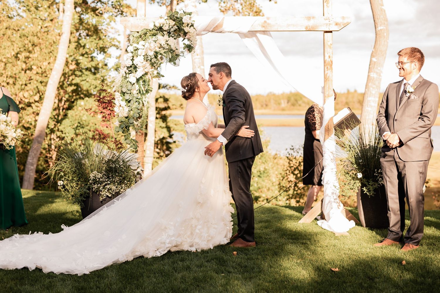 Ceremony under wooden arch with waterfront view and emerald bridesmaids dresses.