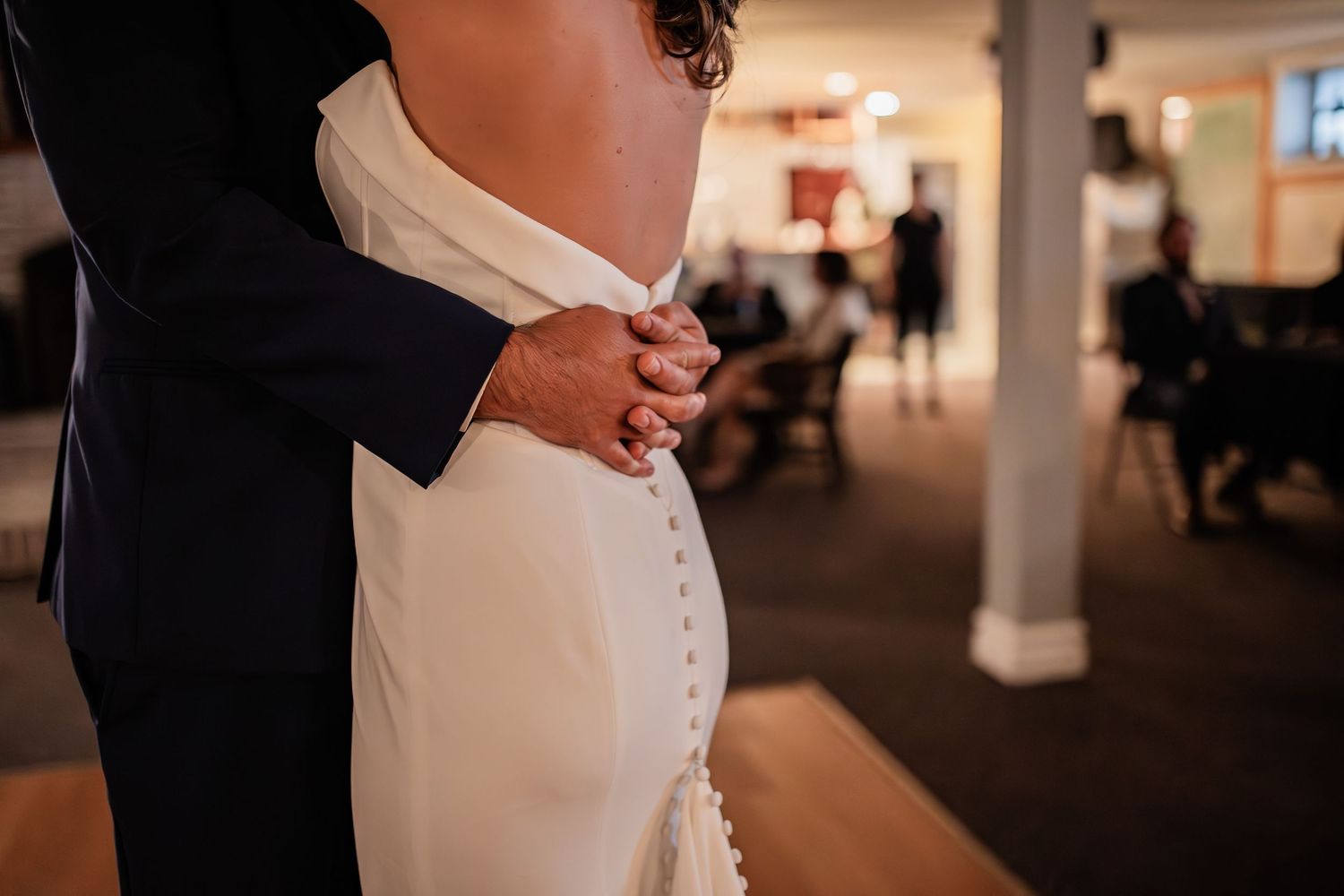 Detail shot of couple embracing during wedding dance showing buttons on bride's fitted gown.