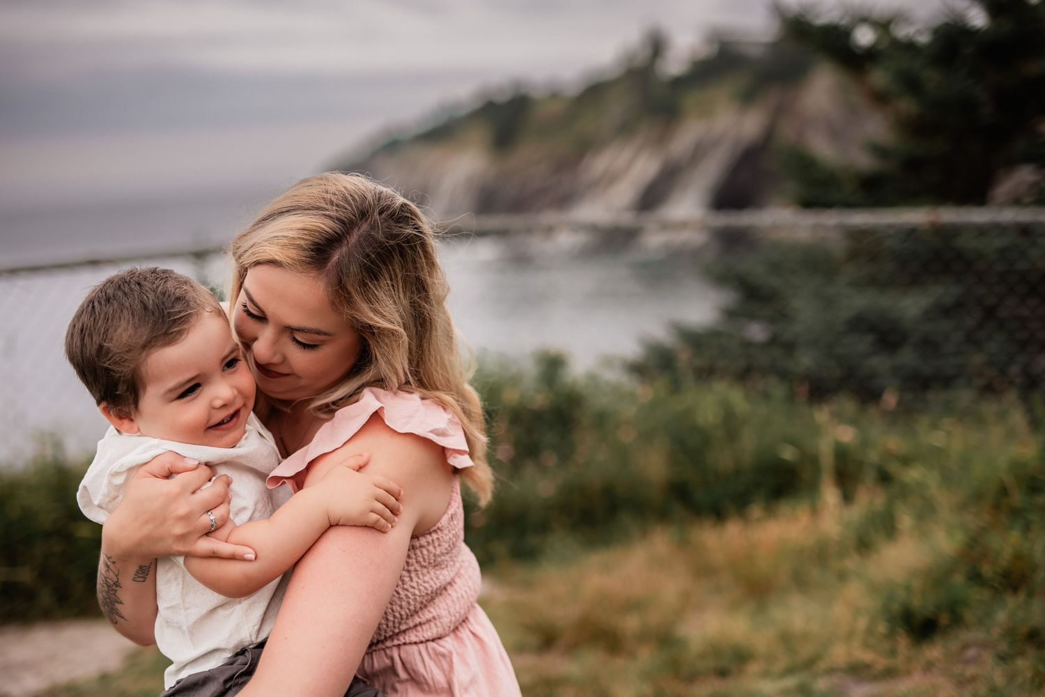 Tender moment between parent and child against coastal landscape background.