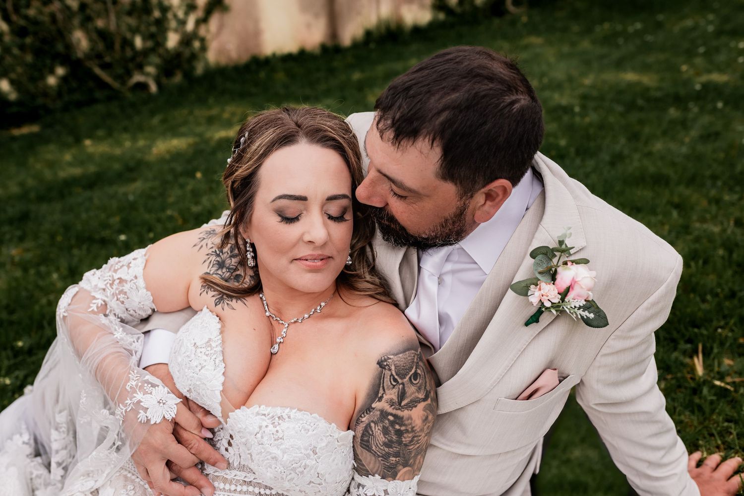 An intimate moment between newlyweds outdoors, with the bride's detailed lace dress and tattoo visible.