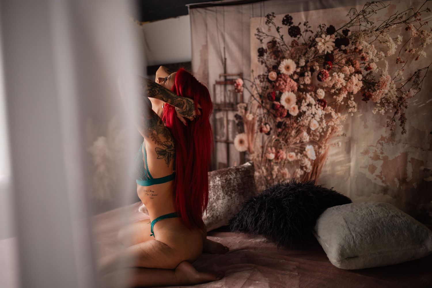 Person in red robe against floral backdrop during intimate boudoir photoshoot.