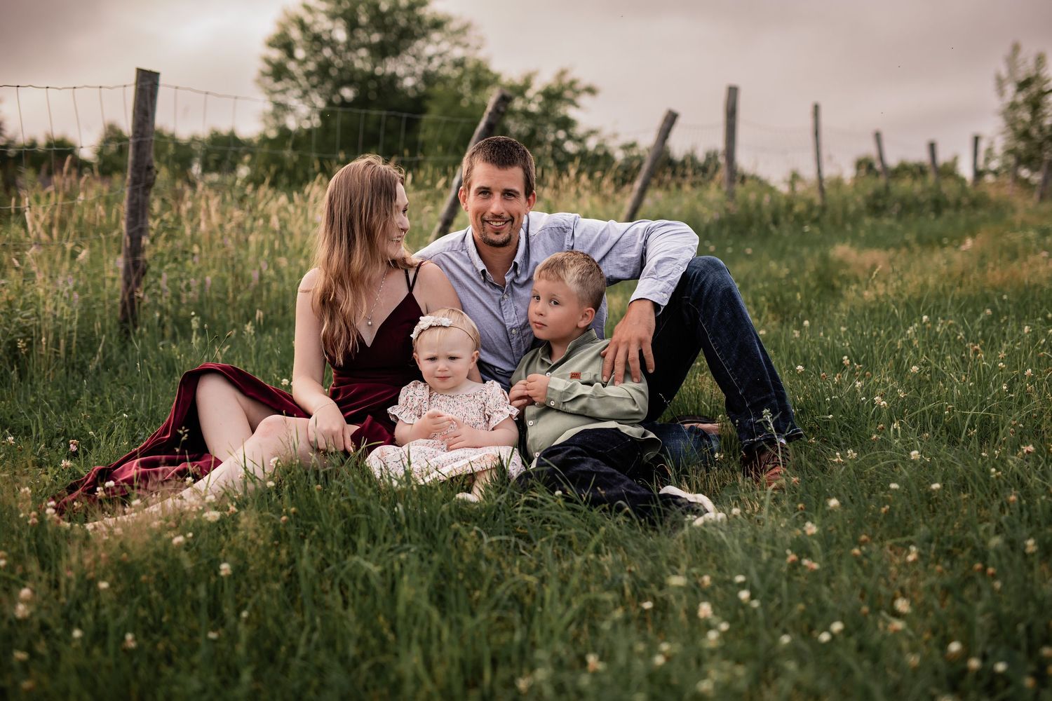 Family relaxing together on blankets in a wildflower meadow at dusk.