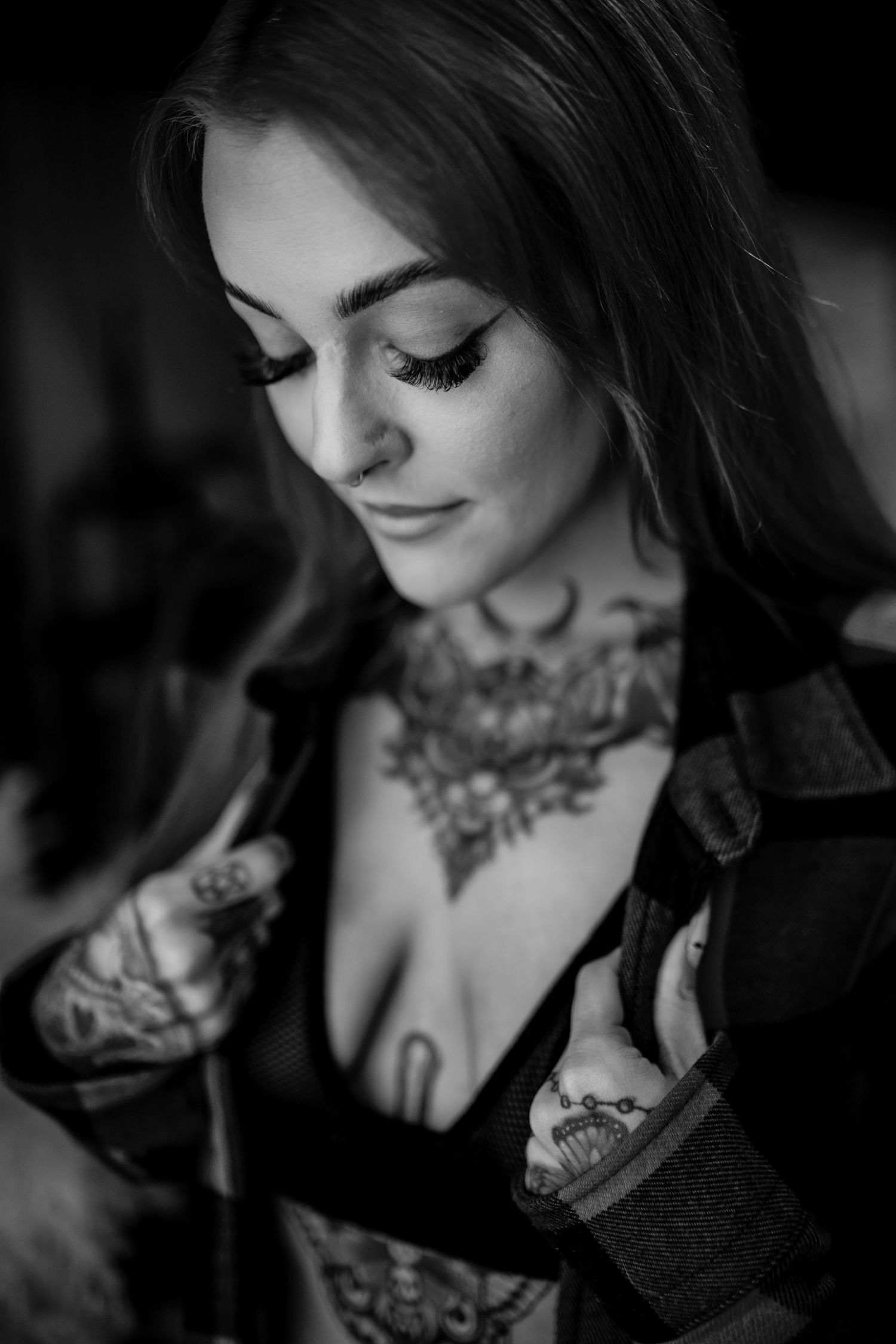 Black and white portrait of person with ornate floral neck tattoos wearing dark clothing.