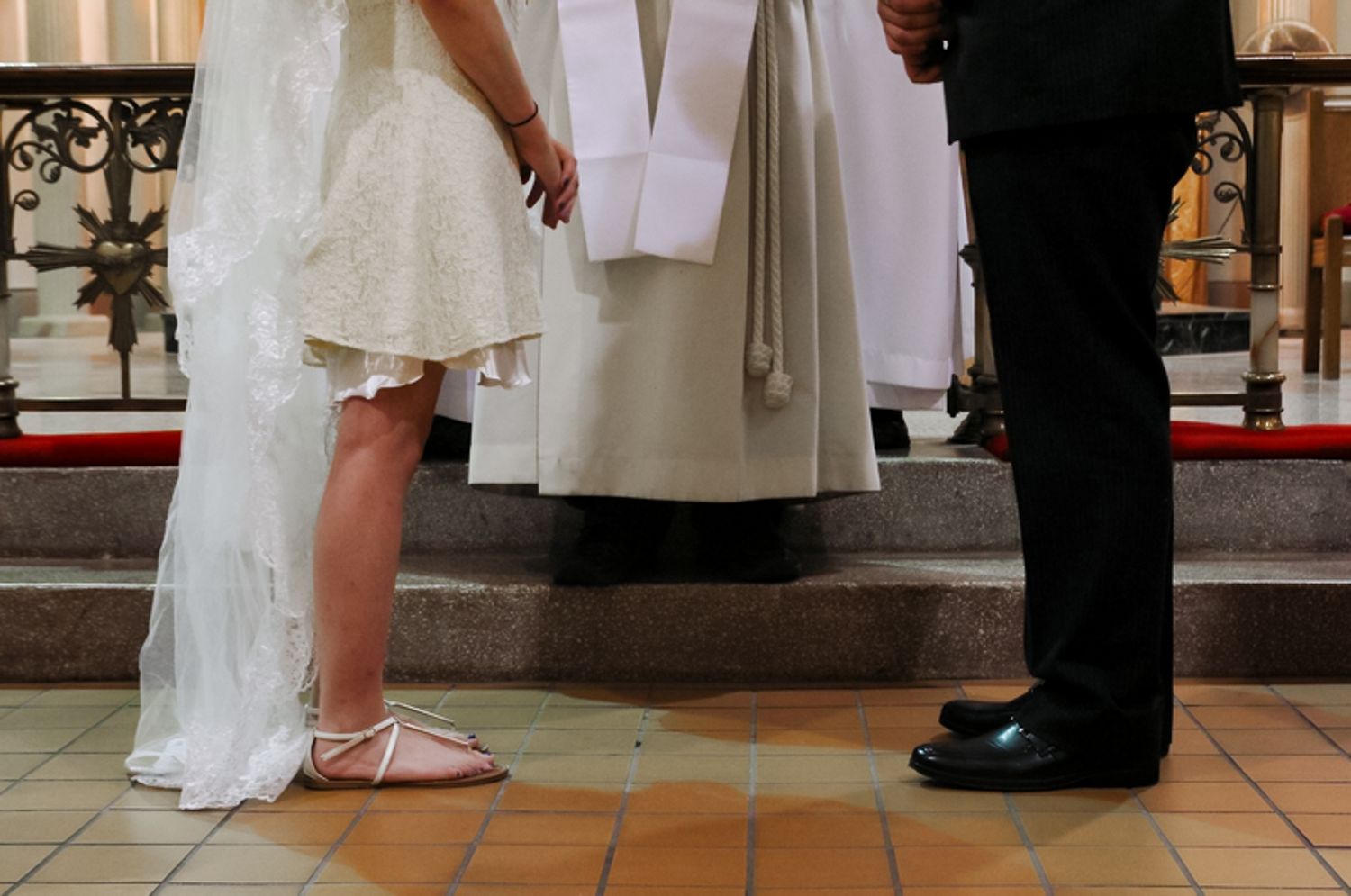Low angle view of bride and groom's feet with priest standing between them during wedding ceremony on tiled floor.
