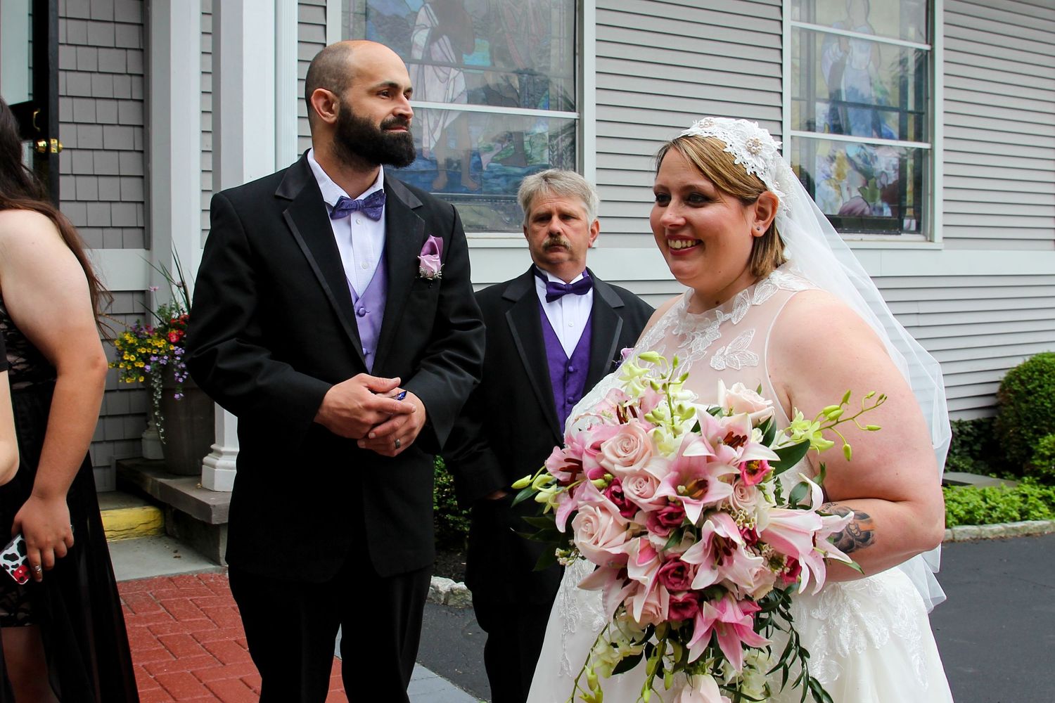Wedding party gathers outside on a sunny day with pink floral bouquet.