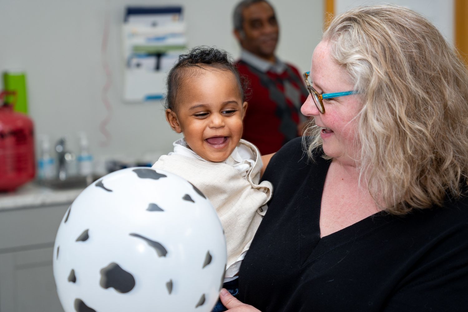 A happy little baby laughing as he plays with a balloon at a birthday party