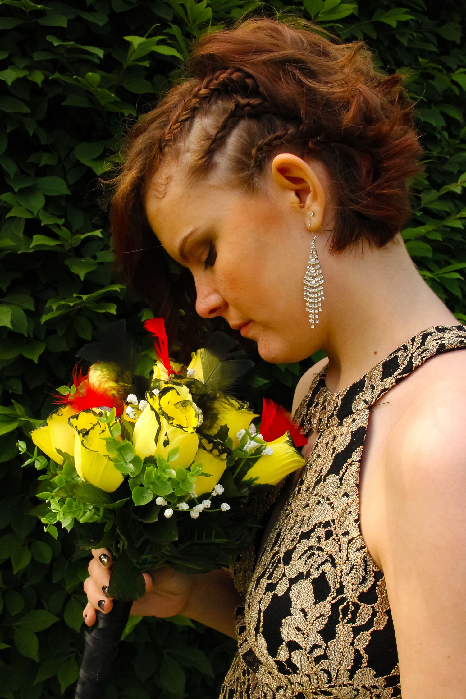 A stylish braided hairstyle shown with an elegant lace dress and floral bouquet against greenery.