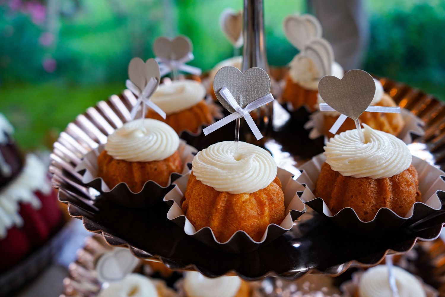 Mini bundt cakes topped with white frosting and heart decorations displayed on a black serving platter.