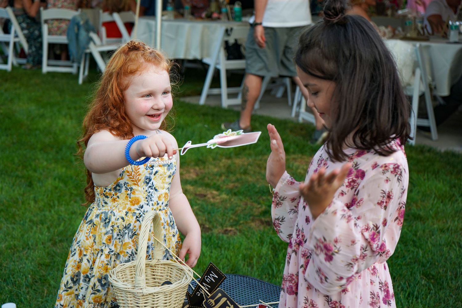 Two young children interact at an outdoor event with one holding a basket.
