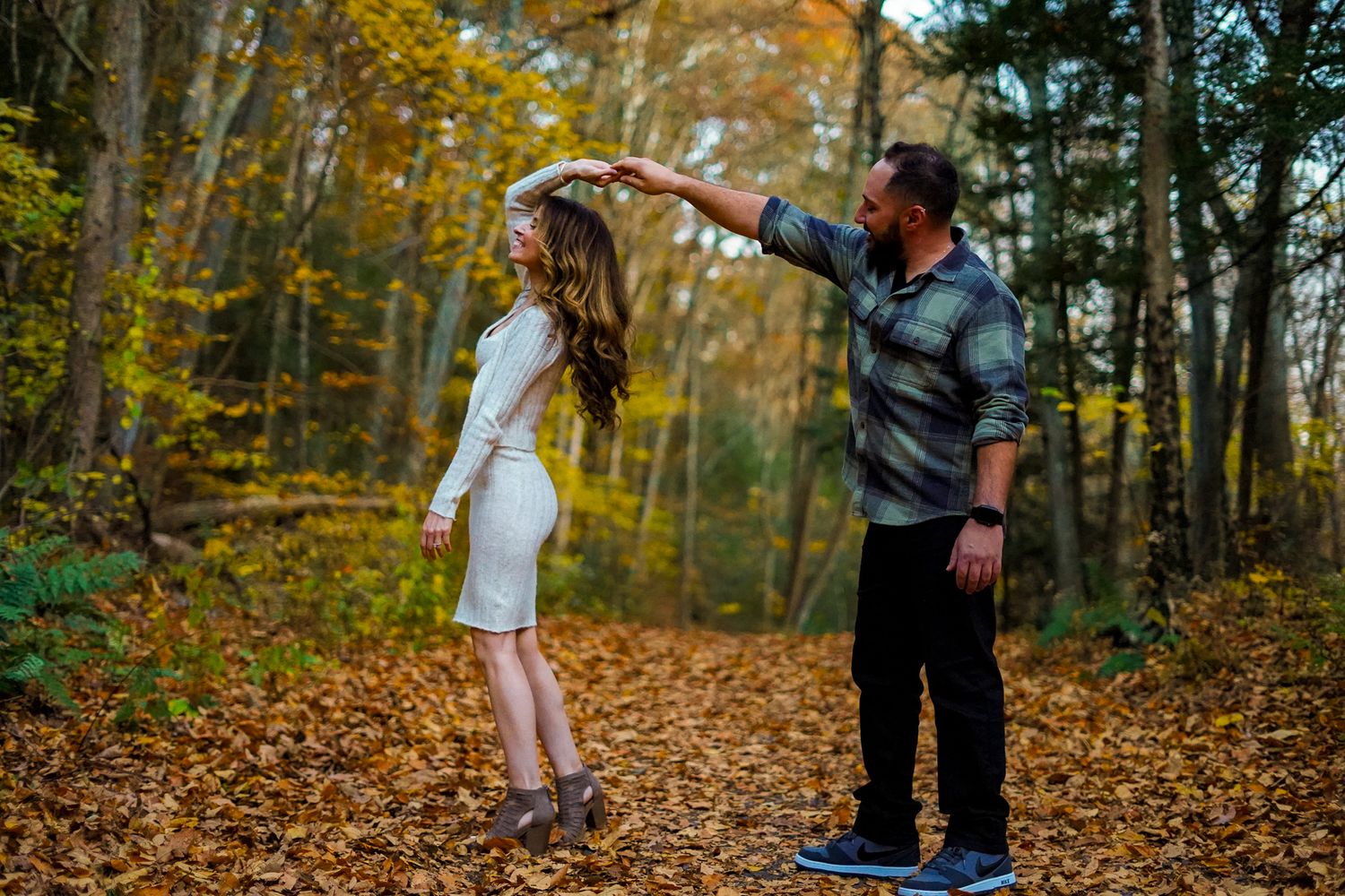 Couple dancing on fallen autumn leaves in forest setting.