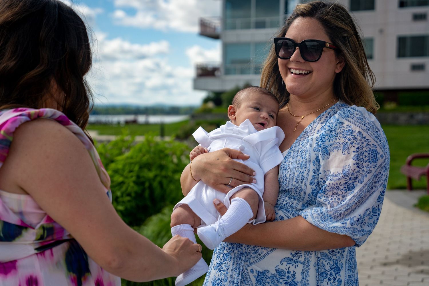People admiring an infant outdoors on a sunny day near modern buildings.