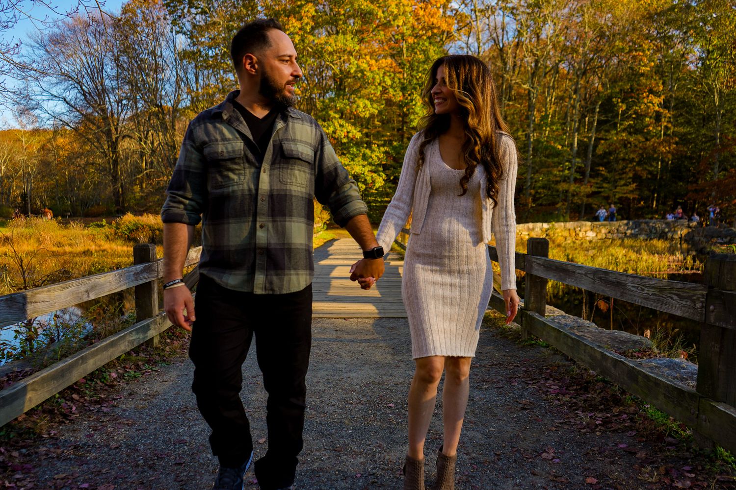 Couple walking together on wooden bridge during fall with colorful foliage in background.