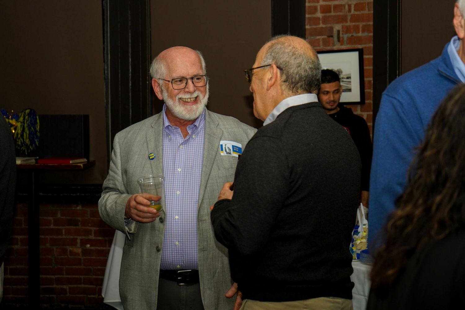 Two older gentlemen having a conversation at an indoor social gathering.