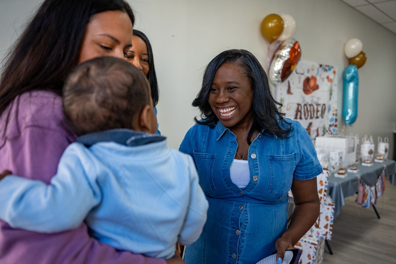 A party guest with a huge smile on her face while interacting with a baby and other guests at a birthday party