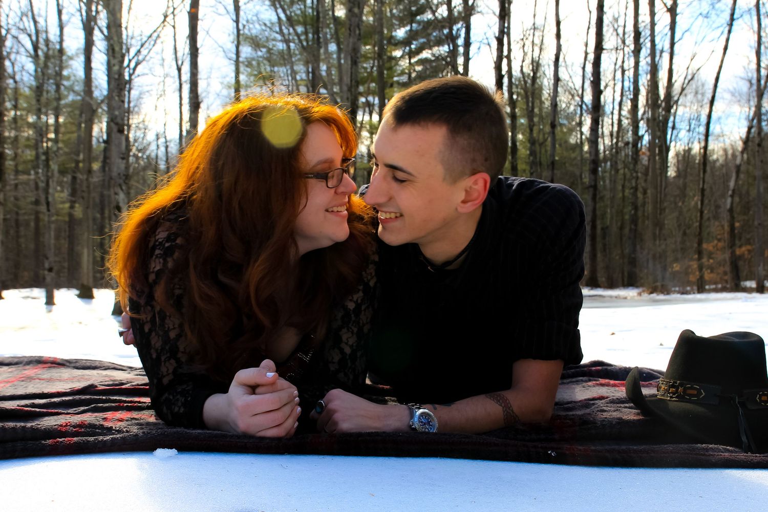 Couple lying on blanket in snowy winter forest setting.