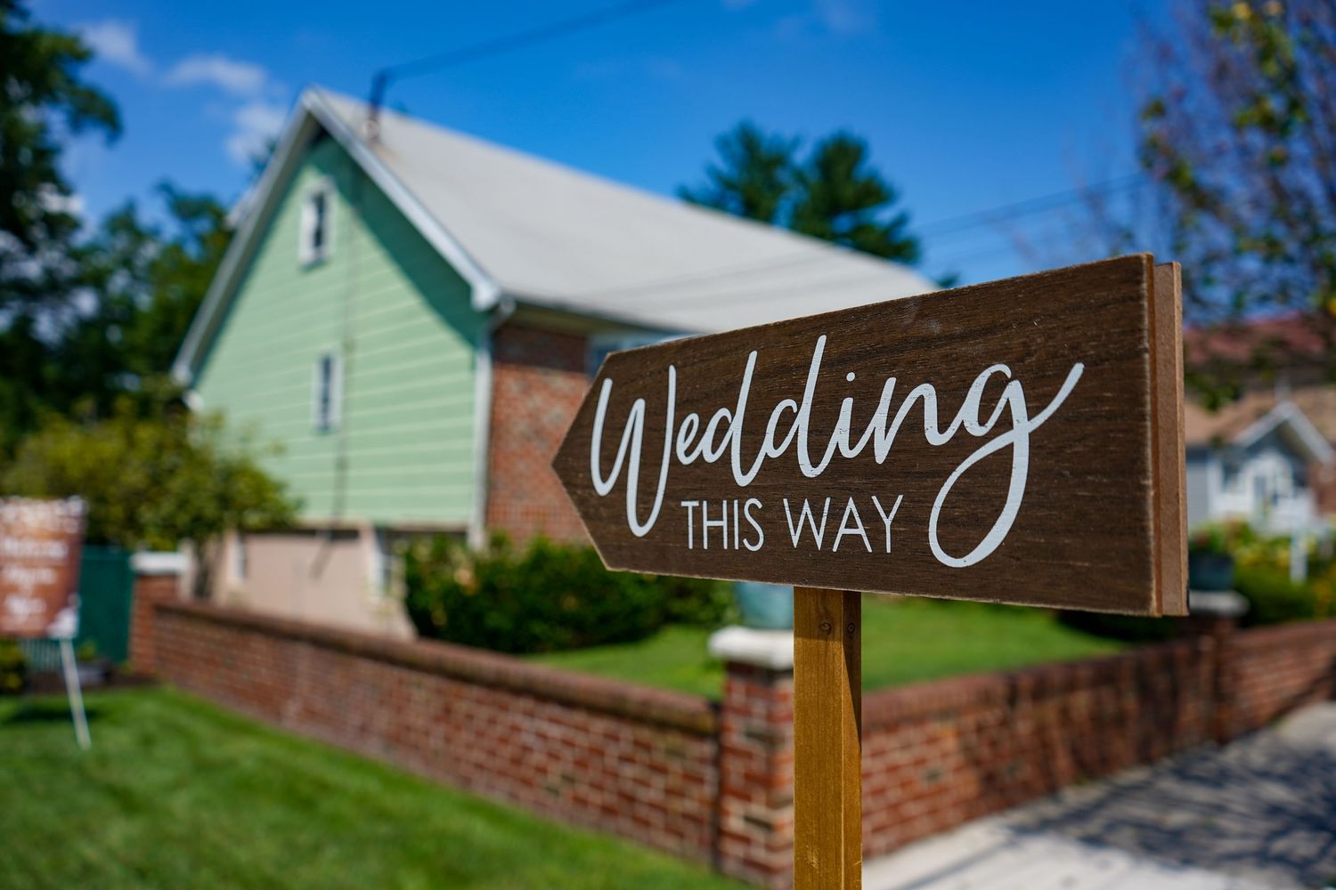 A wooden directional sign reading 'Wedding this way' points toward a mint green house.