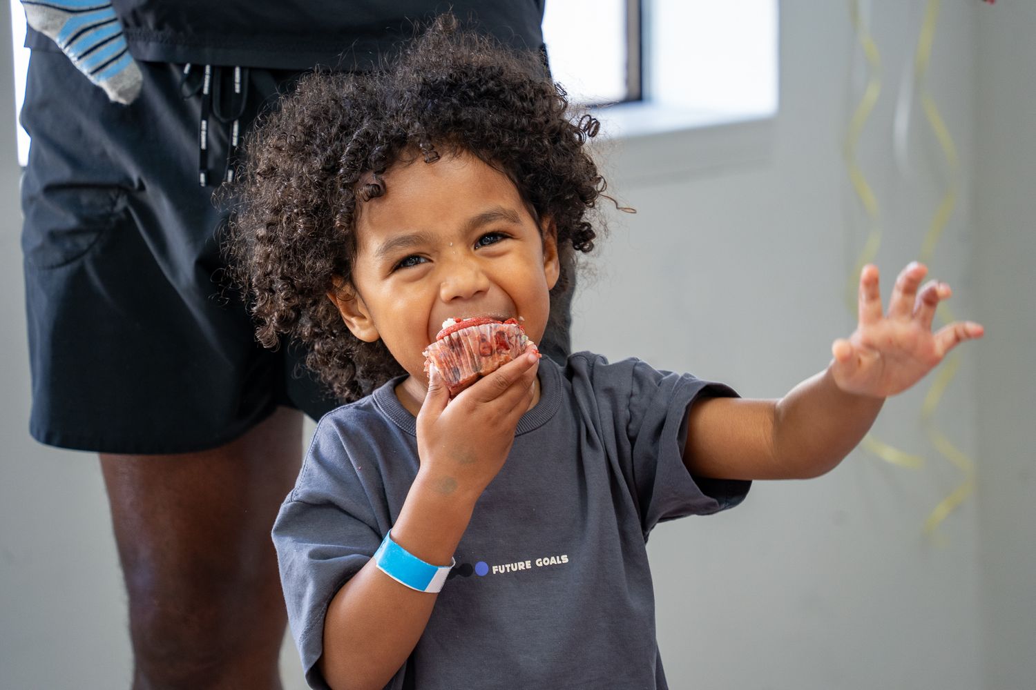 A curly haired little boy happily eating a messy cupcake at a birthday party