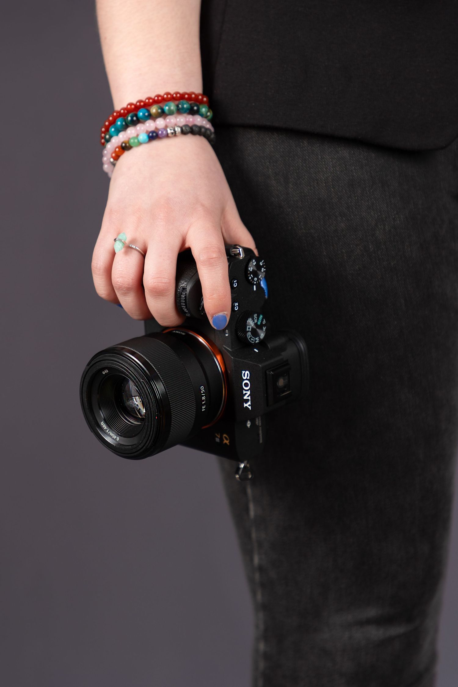 Close-up of colorful beaded bracelets and blue nail polish while holding Sony camera.