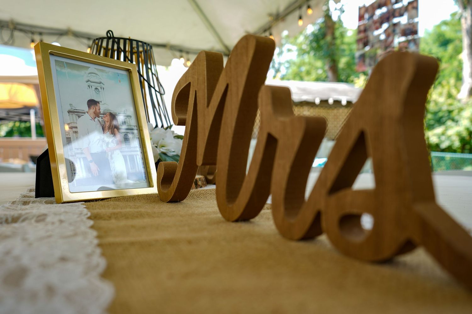 Rustic wooden 'Mrs' wedding table decor letters with photo frame in background.