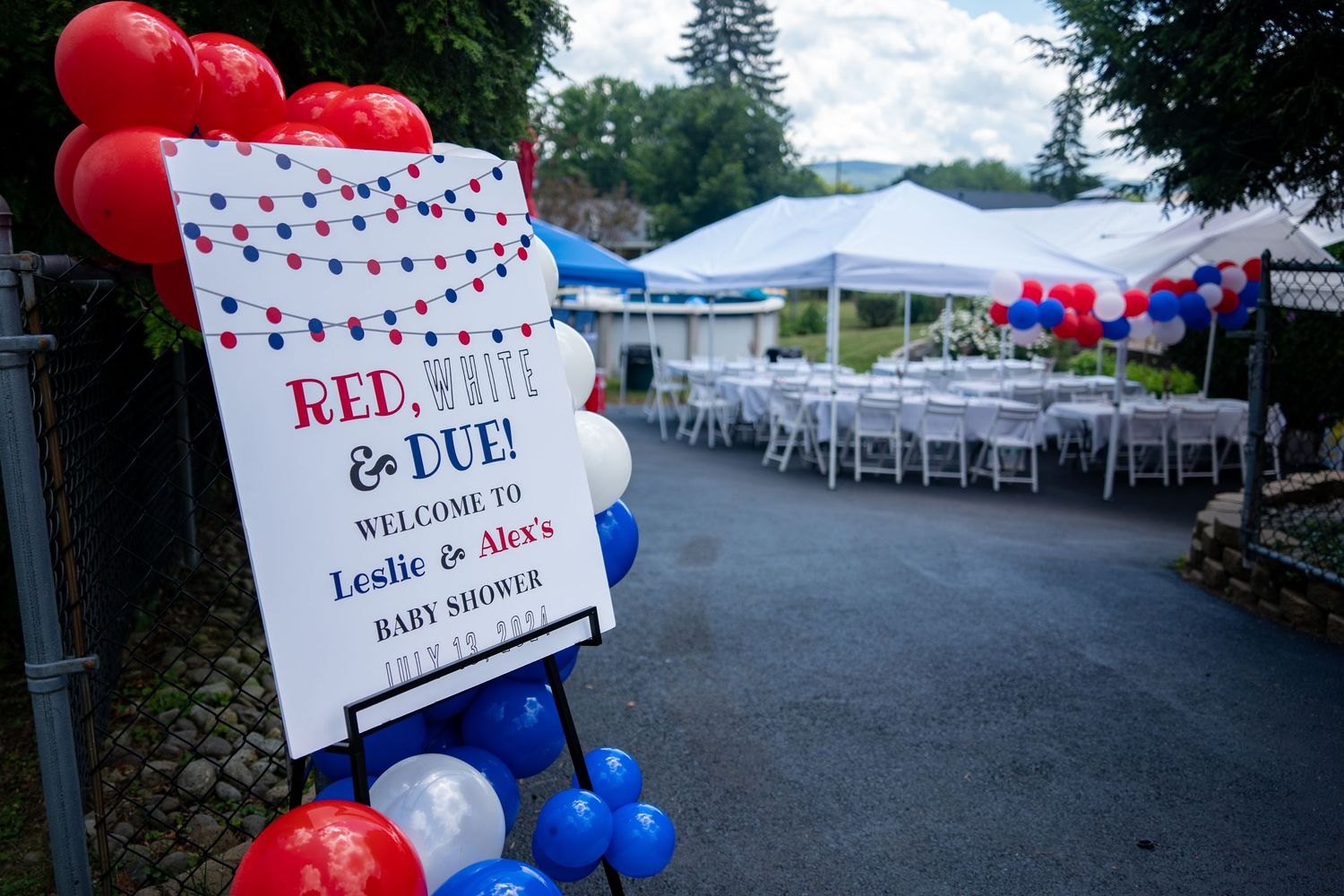Red and blue balloon decorations with a welcome sign for an outdoor event under white tents.