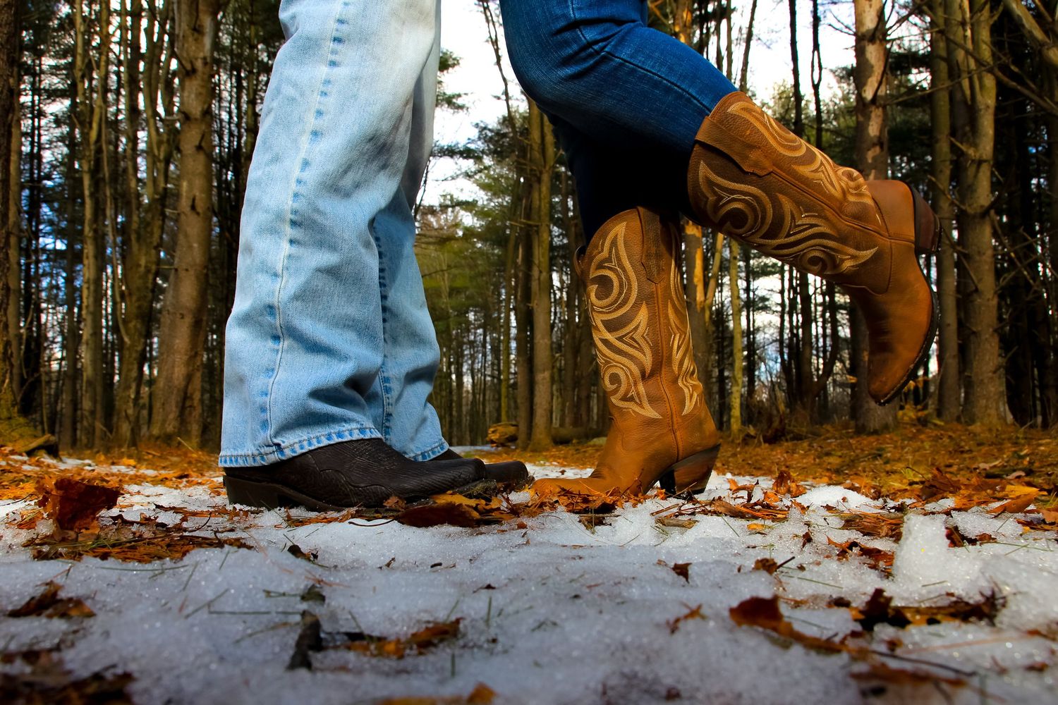 Close-up of cowboy boots and jeans standing in snowy forest.