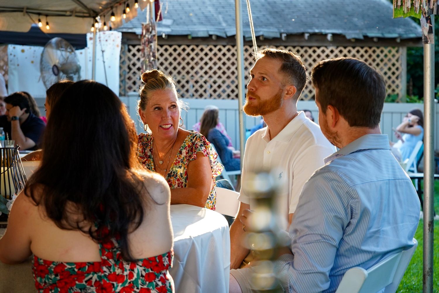 A group of guests socialize and laugh together at an outdoor party under string lights.