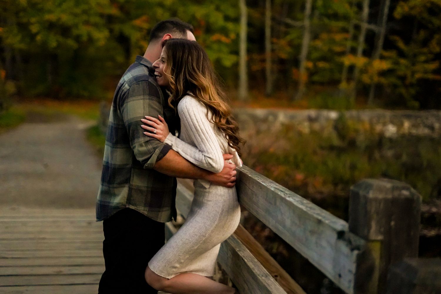 Romantic embrace on wooden bridge during golden hour with fall colors.