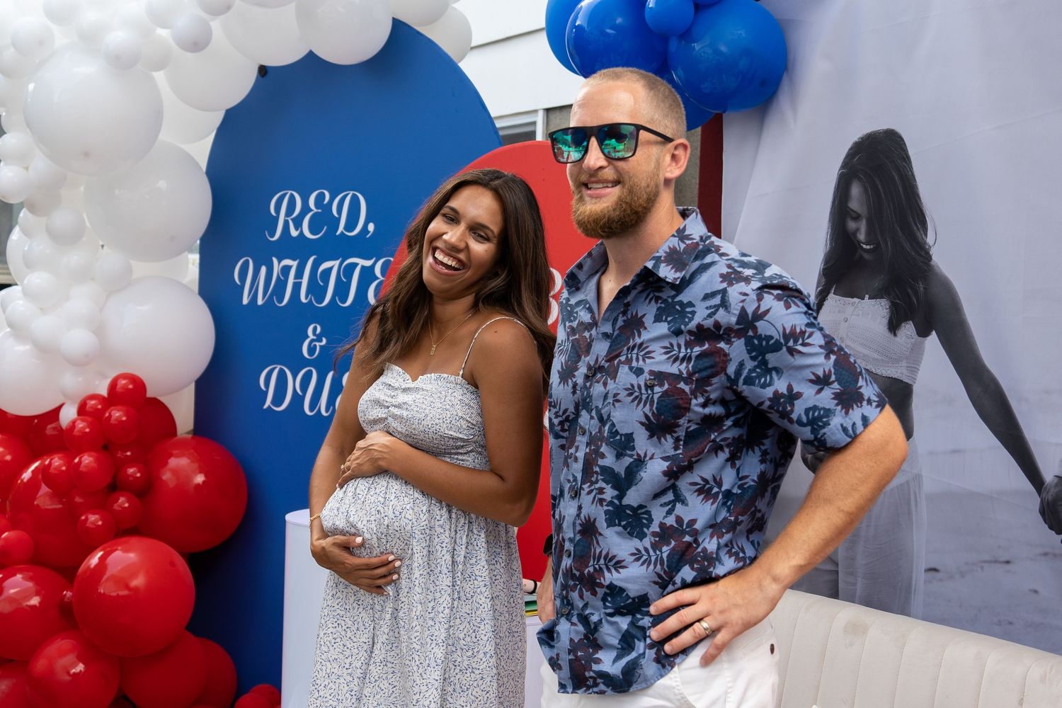 A couple posing in front of a decorated backdrop with balloons at an event.