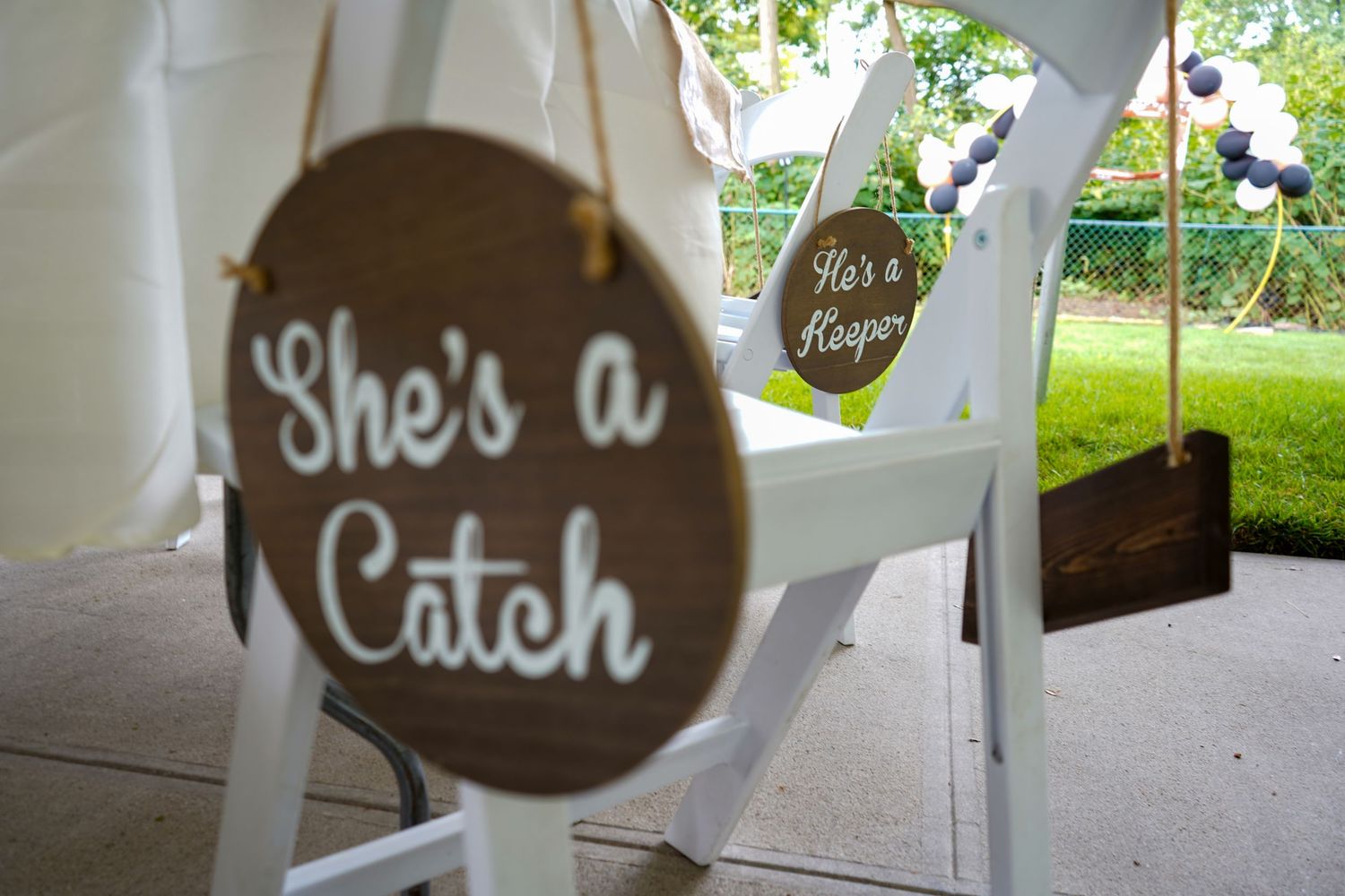Wooden wedding chair sign reading 'She's a Catch' hanging on white seating.