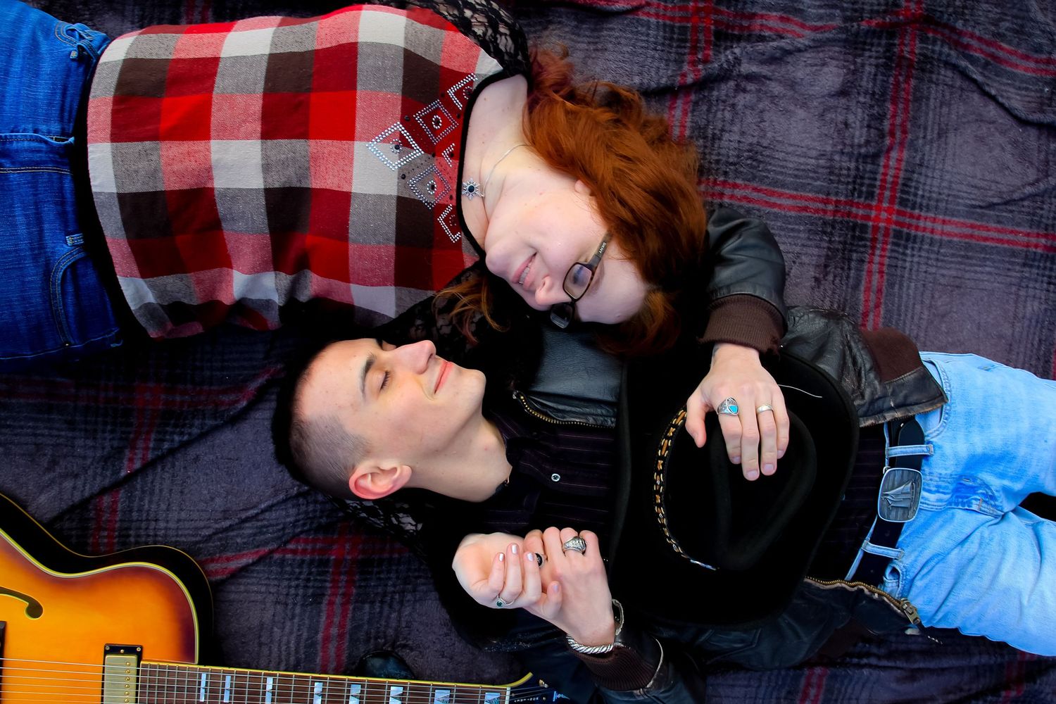 Acoustic guitar lies beside couple on plaid blanket in winter setting.