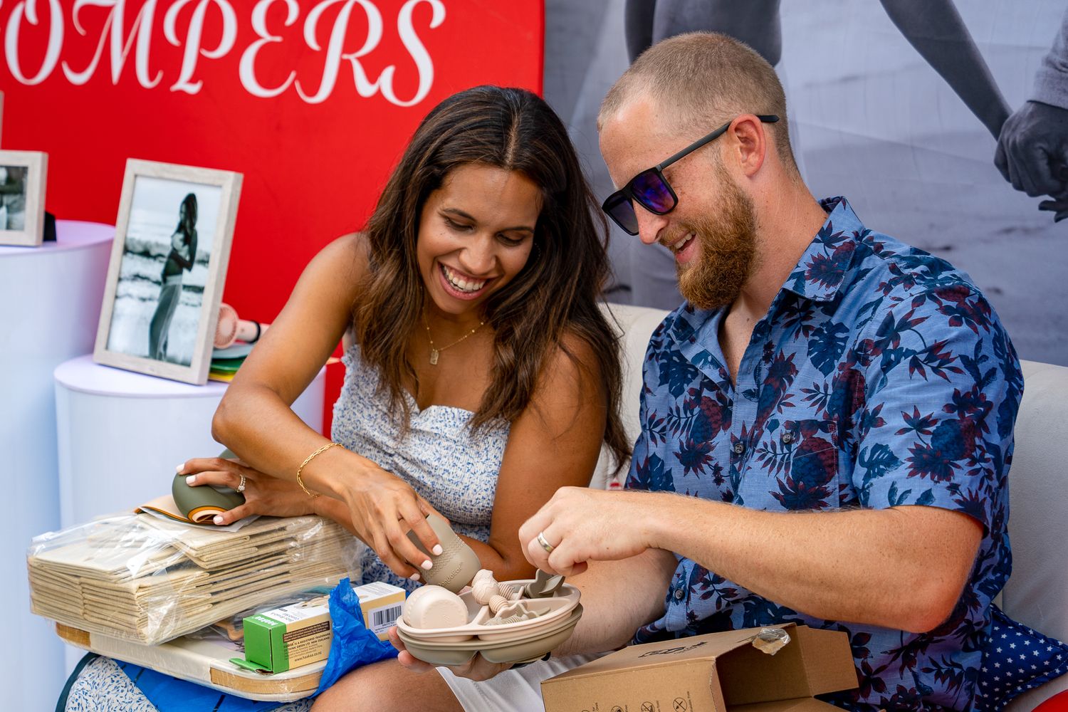 Two people sitting together at a table laughing while crafting or working with pottery materials.