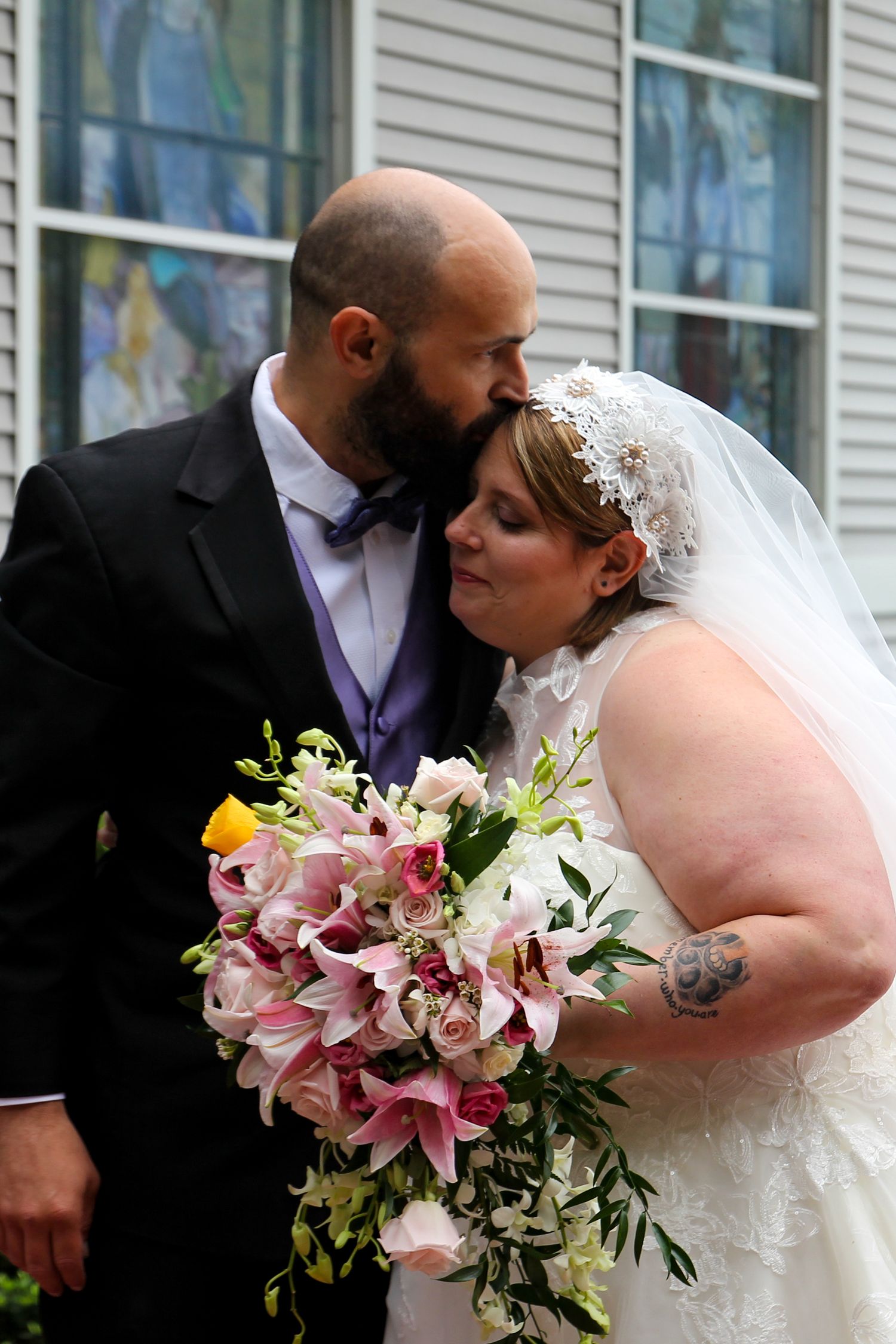 A tender wedding moment shared between newlyweds with a vibrant pink and white lily bouquet.