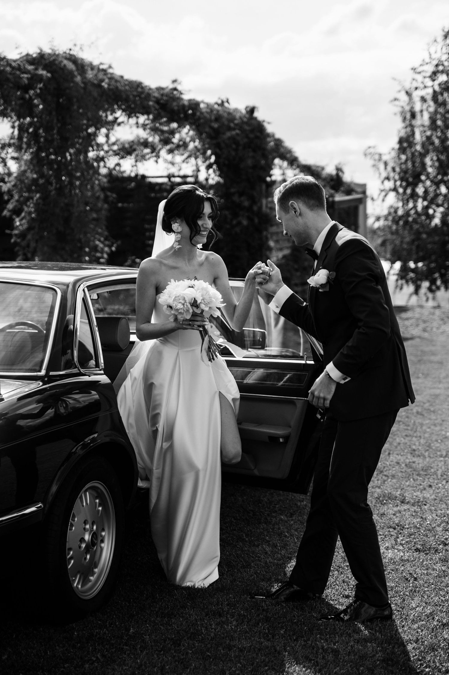 Elegancki ślub w Willi Słonecznej w Dębowcu – pan młody z uśmiechem pomaga pannie młodej wysiąść z klasycznego samochodu do ślubu.