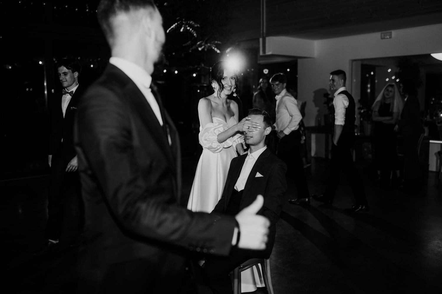 Ujęcie z zabawy weselnej, panna młoda z uśmiechem zasłania oczy ukochanego – filmowa scena z eleganckiego ślubu.