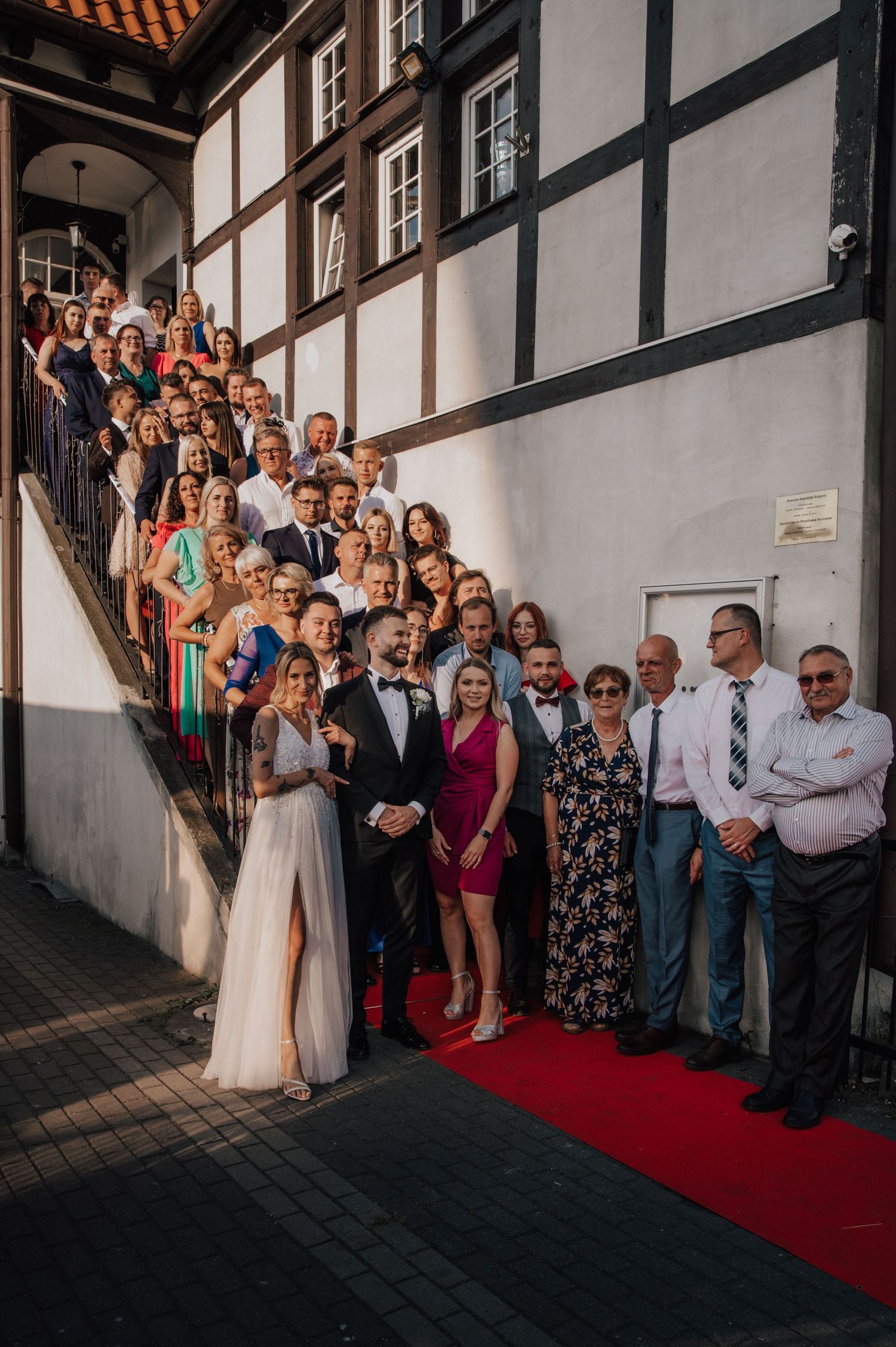 Zdjęcie grupowe gości weselnych z parą młodą na schodach restauracji Ołowianka w Gdańsku.
