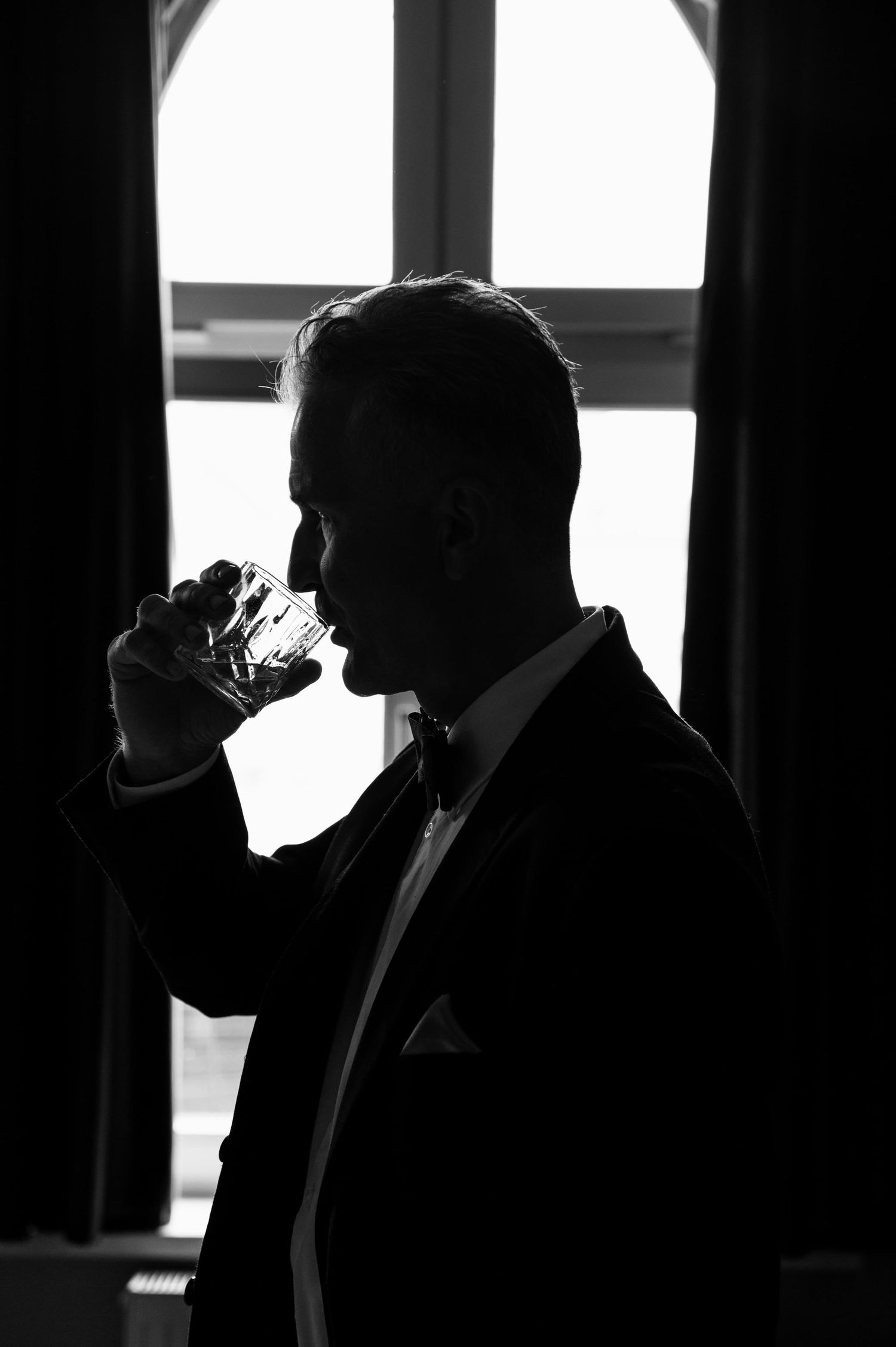 Sylwetka mężczyzny w garniturze pijącego whisky przy oknie.