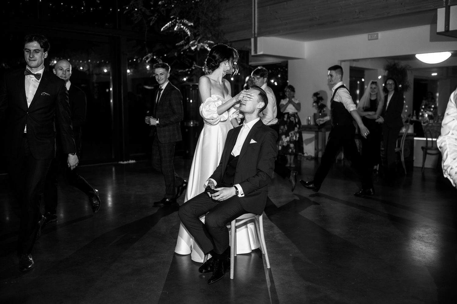 Zabawa weselna z zasłanianiem oczu — rzut muchą, panna młoda i pan młody w eleganckiej, luźnej atmosferze.