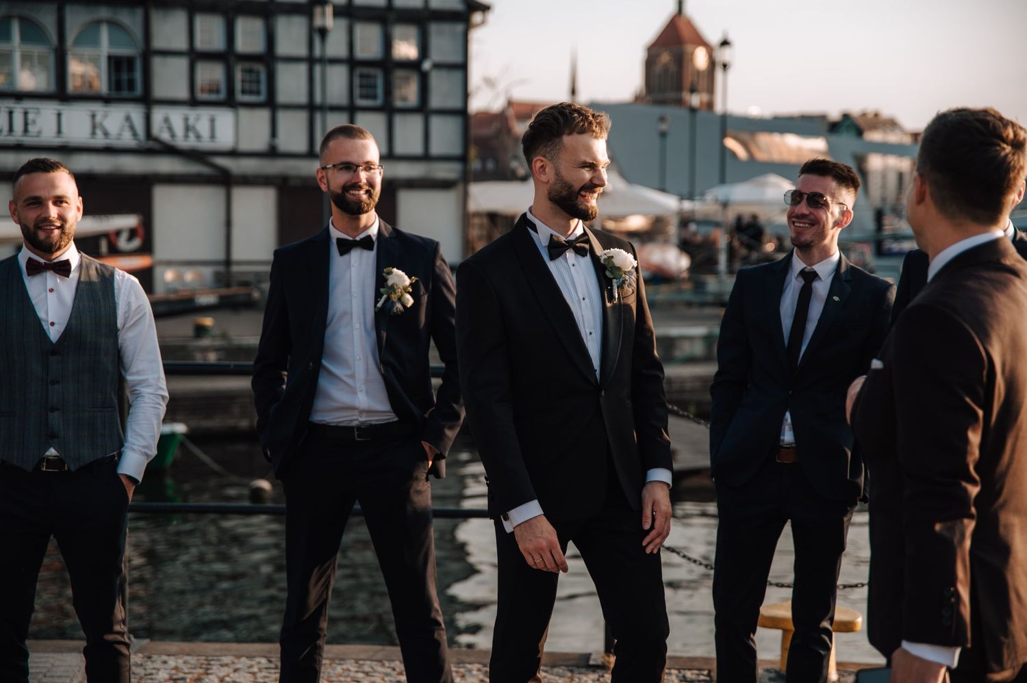Pan młody z drużbami przy nabrzeżu w Gdańsku – elegancki, pełen luzu moment przed zachodem słońca.
