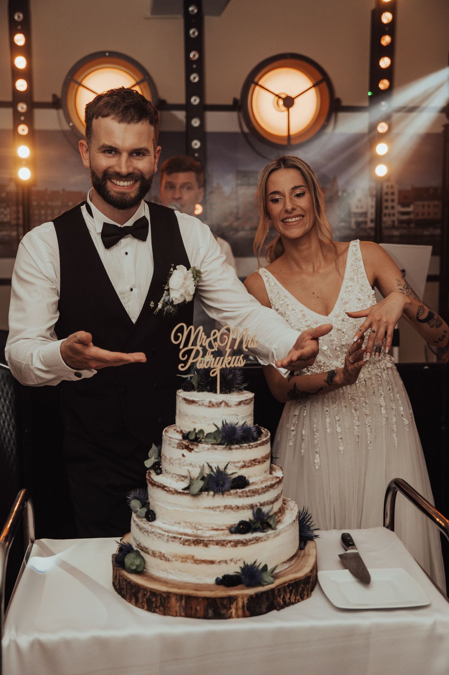 Para Młoda z uśmiechem prezentuje tort weselny — luz, radość i detale dekoracji w stylu rustykalnym