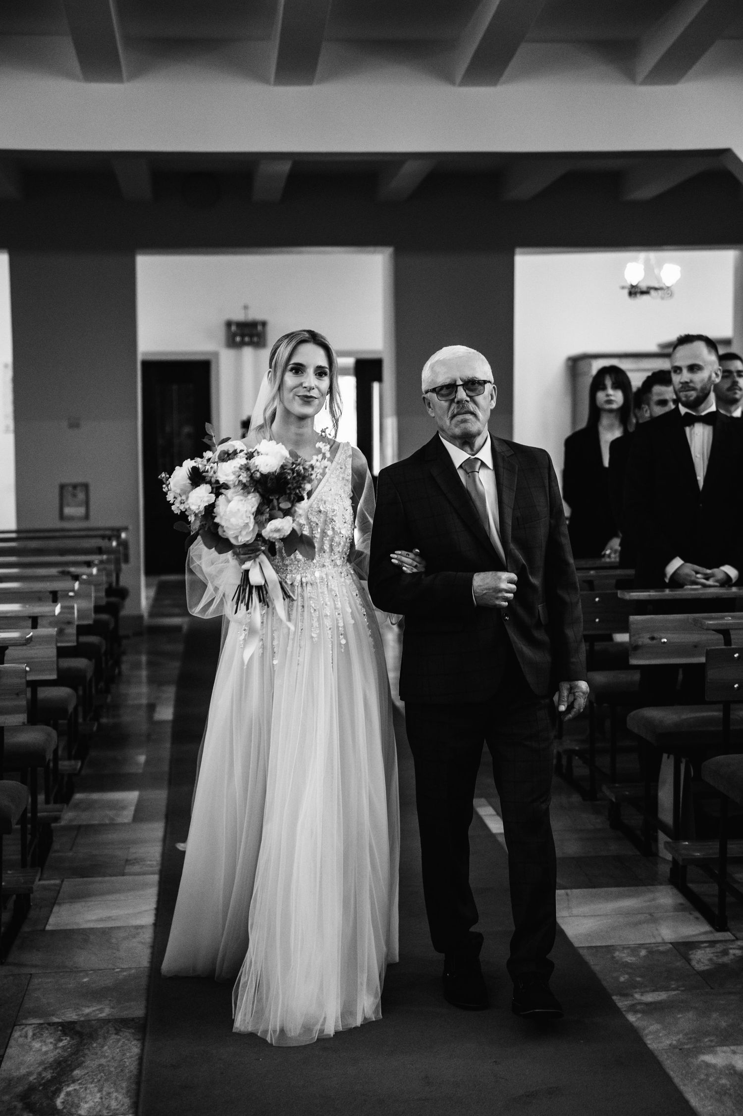Panna młoda prowadzona przez dziadka do ołtarza podczas ceremonii ślubnej.