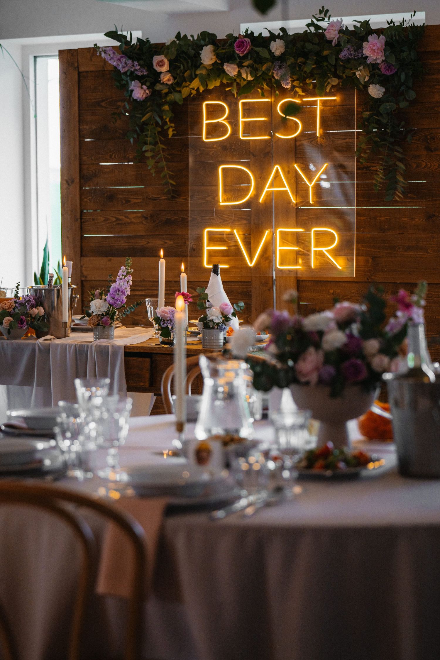 Sala weselna z dekoracjami, kwiatami i napisem neonowym „Best Day Ever”.