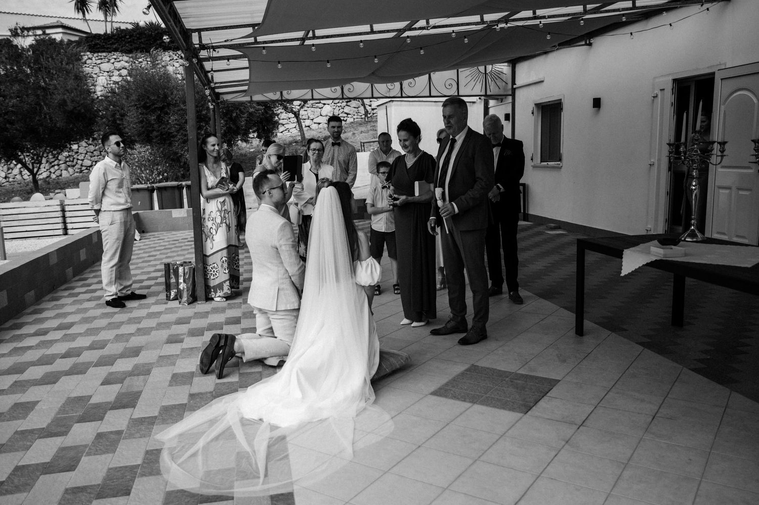Para młoda klęcząca podczas błogosławieństwa w gronie najbliższych – emocjonalny moment przed ceremonią ślubną na Sycylii