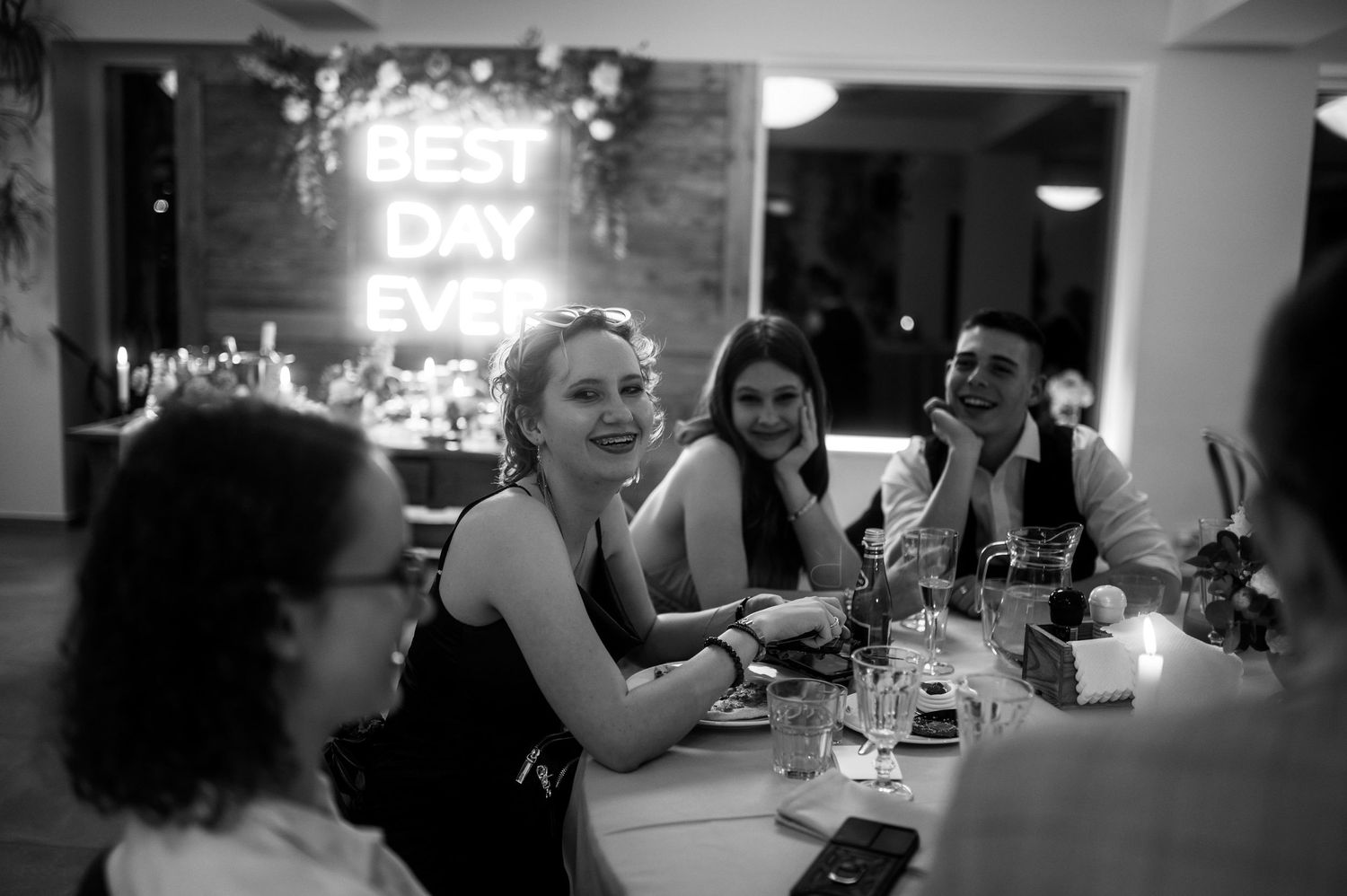 Goście weselni przy stole, śmiejący się w blasku napisu „Best Day Ever” – naturalny, ponadczasowy moment z eleganckiego wesela.