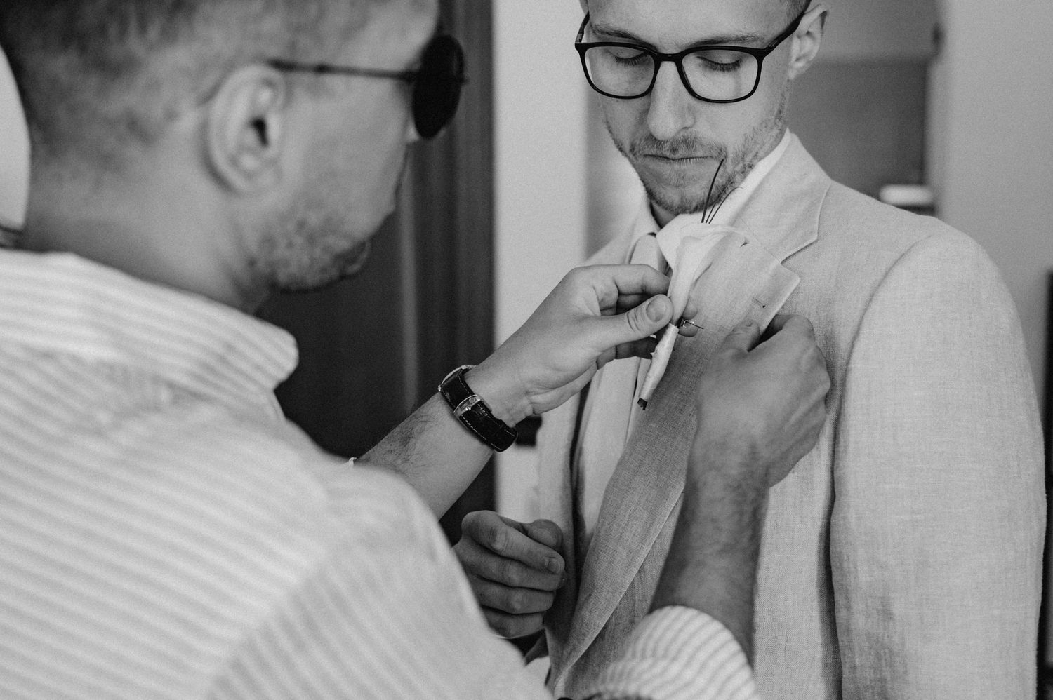 Świadek przypinający boutonniere panu młodemu – elegancki detal przygotowań ślubnych