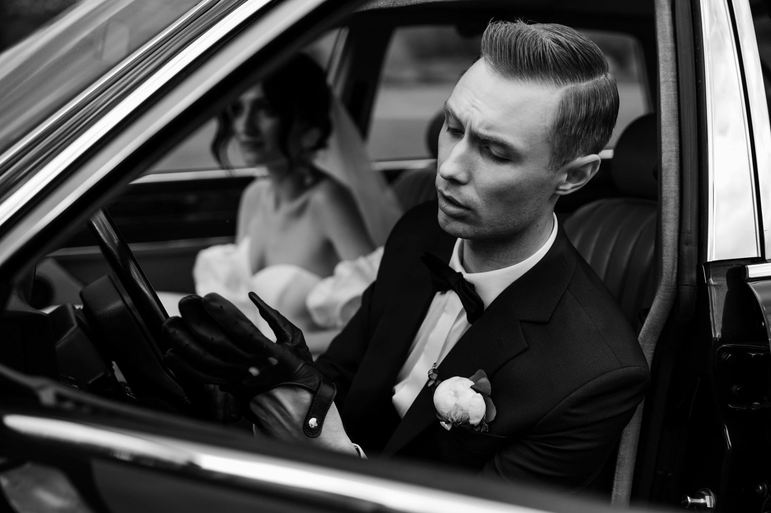 Pan młody w eleganckim garniturze podczas jazdy klasycznym samochodem, elegancki i filmowy klimat reportażu ślubnego