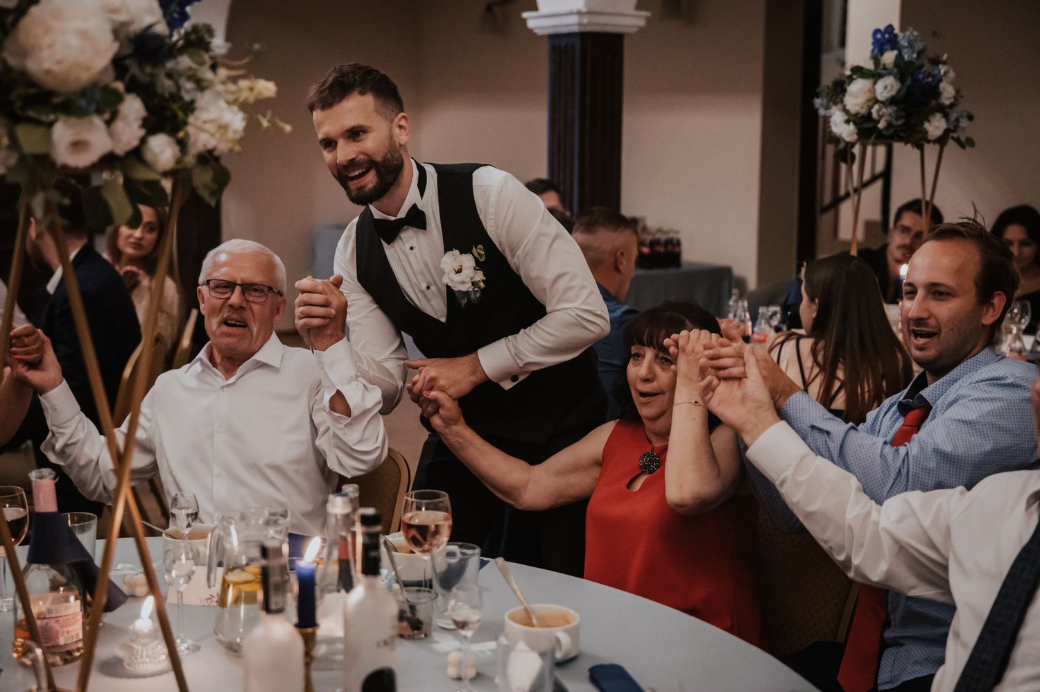 Zabawa weselna — Pan Młody wśród gości, wspólne śpiewy i uśmiechy przy stołach w Restauracji Ołowianka
