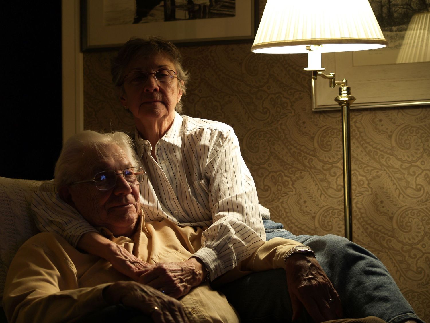 The photo captures an elderly couple sitting together. The man and woman, both with silver hair, wear warm, contented smiles .