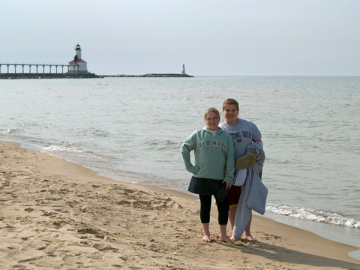 The photo captures a serene moment on a sandy beach with a lighthouse standing tall in the background.