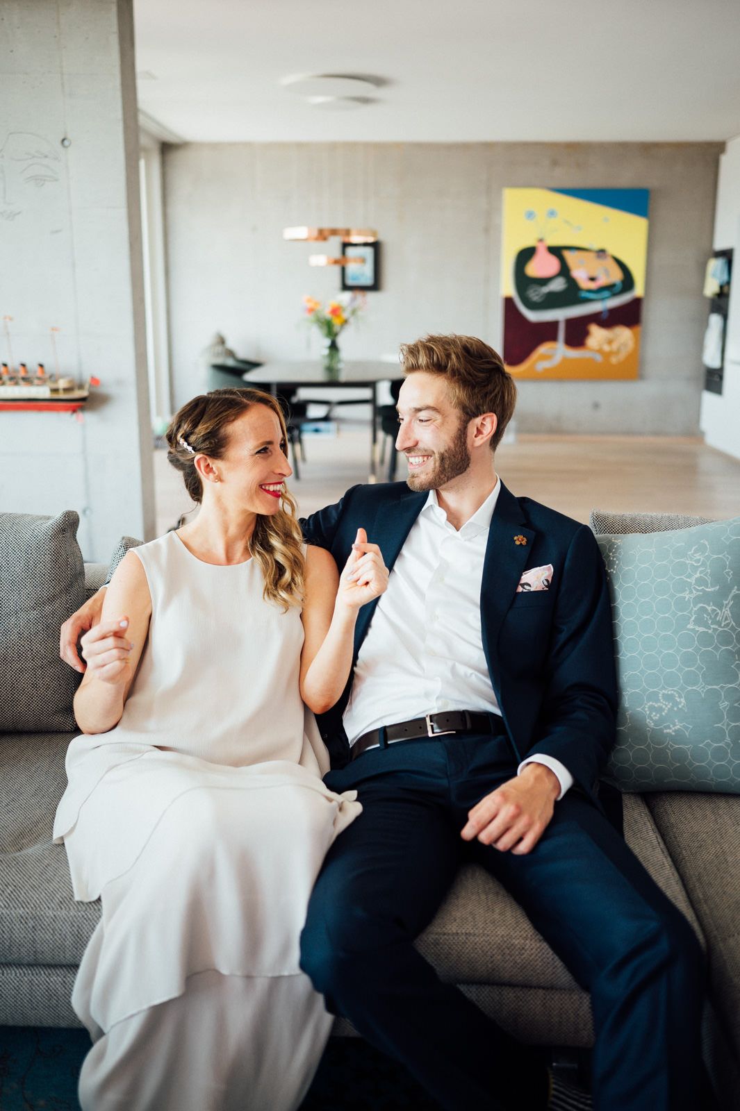 Happy couple relaxing on a gray couch in a modern living room with artwork in the background.
